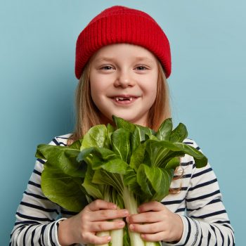 Niña feliz con espinacas en las manos